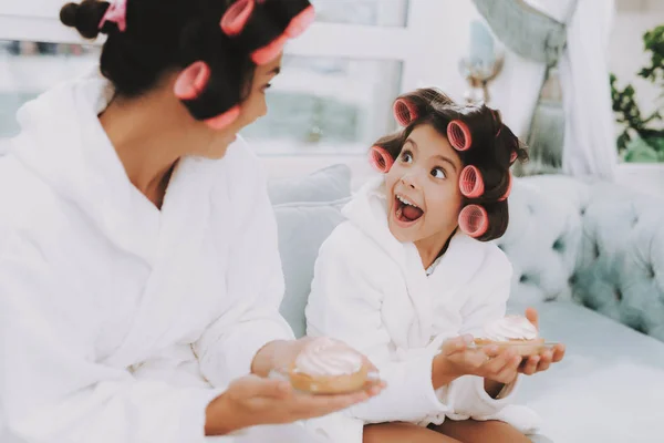 Little Lady with Curlers. Mother and Daughter in Spa. Girl and Mom with Cake. Beautiful Little Lady. Beautiful Face. Woman and Happy Child. Woman with Curlers. Smiling Person. Blue Sofa in Spa Salon.