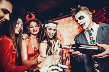 Arkadaşlar Cadılar Bayramı kostümleri şampanya içmek. Dökme şampanya genç adam. Grup Genç arkadaşlar kostümleri giyen içki şampanya gece kulübünde Cadılar Bayramı partisinde olacak