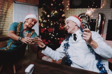 Colleageu fave eğlenceli ofis ile genç doktor. Yeni yıl arifesi. Ofiste Noel ağacı. Bilgisayar masasında. Beyaz ceketli adam. Yeni yıl kutlama. Dijital aygıt kullanarak. Santa Claus Cap.