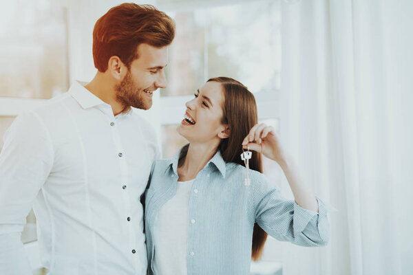 Young Couple Posing In The Bright Room. Buying A Property. Panoramic Windows. Hugging Each Other. Happy Family Relationship. Smiling Together. Sunny Day. Rent A House. Cheerful Sweethearts.