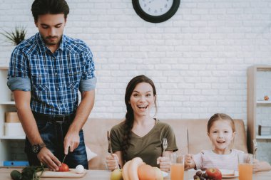 Adam pişirme. Ailece kahvaltı. Kahvaltı mutlu aile. Meyve plaka üzerinde. Ekmek plaka üzerinde. Beyaz tabak. Cam suyu. Yemek masada. Mutlu bir aile. Koltukta oturuyor. Sebze gemide. Beyaz iç.