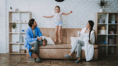 Mutlu aile sabah. Anne ve kızı. Aile birlikte dinlenme. Erkek ve kadın kat olarak. Gülümseyen aile dinlenme. Kız koltukta atlama. Kadın ve adam Kupası ile. Mutlu çocuk ve anne. Beyaz kat.