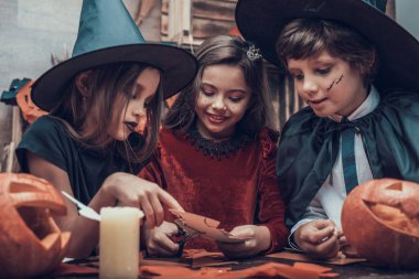 Çocuk kostümleri Halloween süslemeleri yapma. Tablo ve kağıt makas ile kesme renkli parçaları oturan kostümleri çok güzel küçük çocuklar. Genç çocuklar eğlenceli Cadılar Bayramı kutlama sahip