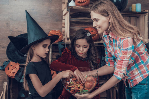 Woman gives Candys to Kids in Halloween Costumes. Happy Halloween Party with Children Trick or Treating. Young Adorable Girls having Fun and getting Sweets. Celebration of Halloween
