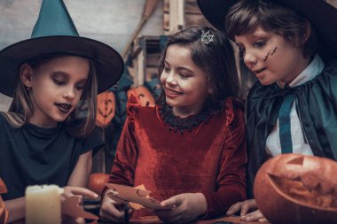 Çocuk kostümleri Halloween süslemeleri yapma. Tablo ve kağıt makas ile kesme renkli parçaları oturan kostümleri çok güzel küçük çocuklar. Genç çocuklar eğlenceli Cadılar Bayramı kutlama sahip