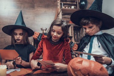 Çocuk kostümleri Halloween süslemeleri yapma. Tablo ve kağıt makas ile kesme renkli parçaları oturan kostümleri çok güzel küçük çocuklar. Genç çocuklar eğlenceli Cadılar Bayramı kutlama sahip