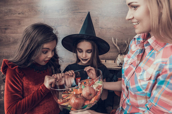 Woman gives Candys to Kids in Halloween Costumes. Happy Halloween Party with Children Trick or Treating. Young Adorable Girls having Fun and getting Sweets. Celebration of Halloween