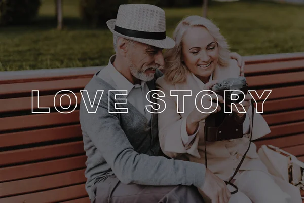 Love Story. Vintage Camera. Photos. Leisure Time. Two Pensioners. Smiling. Have Fun. Happy Together. Bubbly Relationships. Hugs. Alley in Park. Old Couple. Sit. Elderly Man. Woman. Gift. Retired.