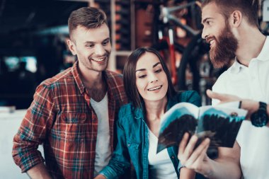 Genç çift Danışmanı ile yeni bisiklet seçin. Gülümseyen adam ve mutlu kadın gözden dikkatle öğretim veya katalog farklı bisiklet ve ayrıntıları içerir. Spor mağazasında tezgâhtar yardımcı olur