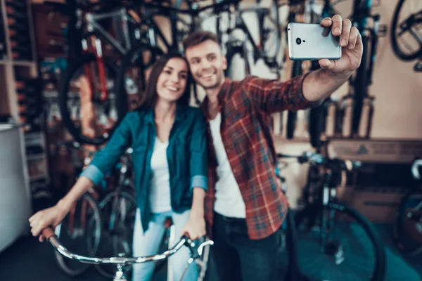 若い男と女は 自転車店で Selfie を作る 幸せな笑顔のカップルは スポーツ サイクルのワーク ショップで子供自転車を選択します 女性がスマート フォンにハンドルと男に写真を保持します — ストック写真
