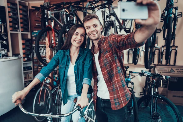 若い男と女は 自転車店で Selfie を作る 幸せな笑顔のカップルは スポーツ サイクルのワーク ショップで子供自転車を選択します 女性がスマート フォンにハンドルと男に写真を保持します — ストック写真