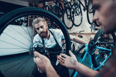 İki adam closeup bisiklet spor atölyede tamir. Cycle Store'a genç gülümseyen adam Modern Bisiklet tamir profesyonel tamirci yardımcı oldu. Bisiklet bakım ve spor salonu konsept