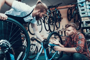 İki adam bisiklet spor atölye inceleyin. Cycle Store'a genç gülümseyen adam Modern Bisiklet tamir profesyonel tamirci yardımcı oldu. Bisiklet bakım ve spor salonu konsept