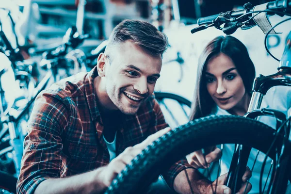 少女と男は スポーツ店でバイクのホイールに見えます 幸せのコンサルタントは スポーツ ショップと密接に詳細を見て購入するサイクルを示しています 若い女性店員のクローズ アップは バイクを選ぶ際に役立ちます — ストック写真
