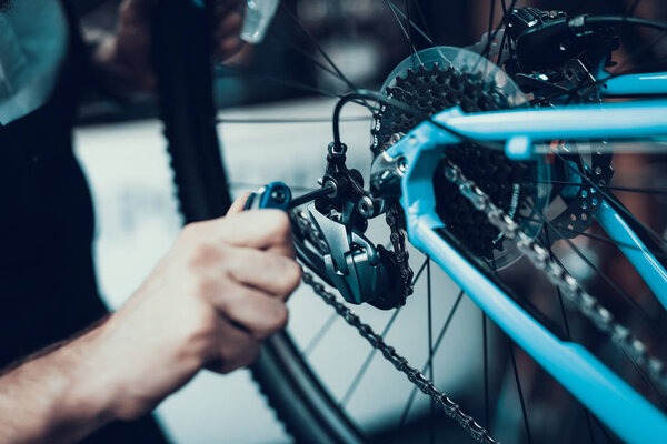 Mechanics Hand Repairing Bicycle in Bike Workshop. Closeup of Male Muscular Hand Examining and Fixing Modern Cycle Transmission System. Bike Maintenance and Sport Shop Concept