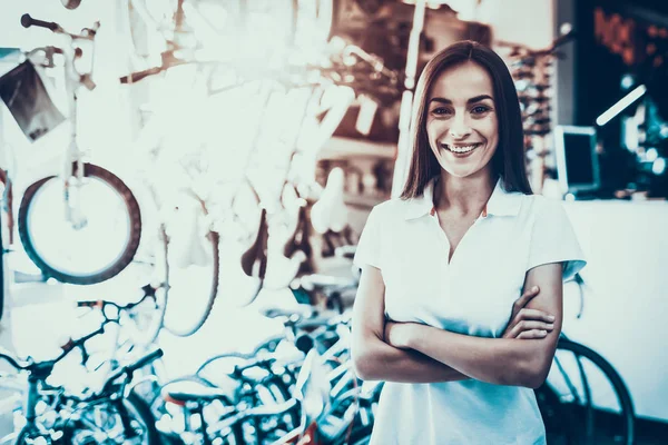 Female Seller with Crossed Hands in Cycle Shop. Portrait of Cheerful Smiling Caucasian Woman Wearing White T-Shirt Looking at Camera Standing Near Bicycles and Poses in Workshop