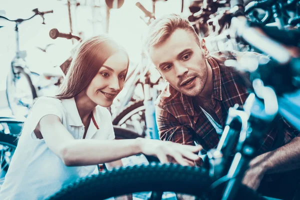 少女と男は スポーツ店でバイクのホイールに見えます 幸せのコンサルタントは スポーツ ショップと密接に詳細を見て購入するサイクルを示しています 若い女性店員のクローズ アップは バイクを選ぶ際に役立ちます — ストック写真