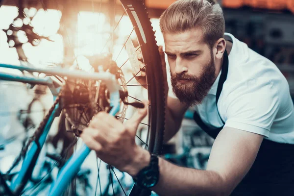 Handsome Bike Mechanic Repairs Bicycle in Workshop. Closeup Portrait of Young Bearded Guy Wearing White T-Shirt Fixes Modern Cycle Transmission System. Bike Maintenance and Sport Shop Concept