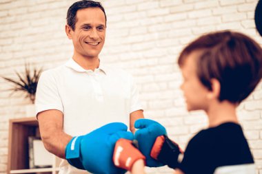 Baba ve oğul lekelenme. Evde spor. Yukarı üç aylık dönemde sıcak. Birbirimize selamlıyorum. Kırmızı ve mavi boks eldivenleri. Spor yapıyor. Adam ve oğlan tren. Boks eldivenleri dairesinde çocuk. Consept sağlıklı.