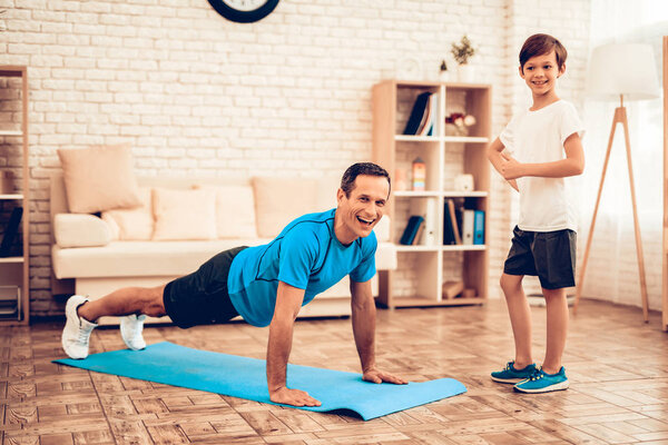 Boy Standing on Scales. Father and Son do Spotting. Sport at Home. Warm Up in Quarter. Lying on Gymnastic Mat. Dumbbells in Hands. Boxing Gloves. Doing Sports. Man and Boy Train at Home. Swing Press. 