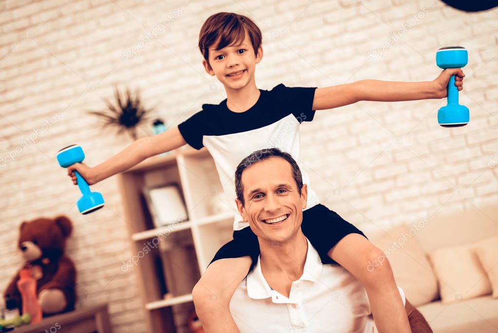 Man and Son Sitting on Sofa. Sports for Disabled. Man with Dumbbells in Hands. Boy with Dumbbells in Hands. Father and Boy Do Spotting. Sport at Home. Health Concept. Healthy Lifestyle. White Interior