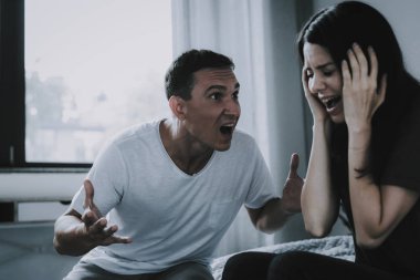 Angry Husband Screams at Wife During Quarrel. Woman Holds Head with Hand Has Conflict with Man at Home. Married Couple Sitting on Bed and Arguing. Family Relationship Problems and Misunderstanding clipart