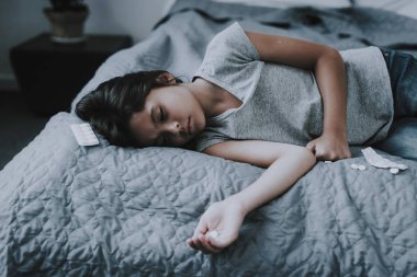 Kız yatakta tabletler ve yalan büyük doz aldı. Küçük koyu saçlı beyaz Indiffenent çocuk birkaç hap ilaç açılan ambalaj yakınındaki gri Badcover yatan elinde tutan