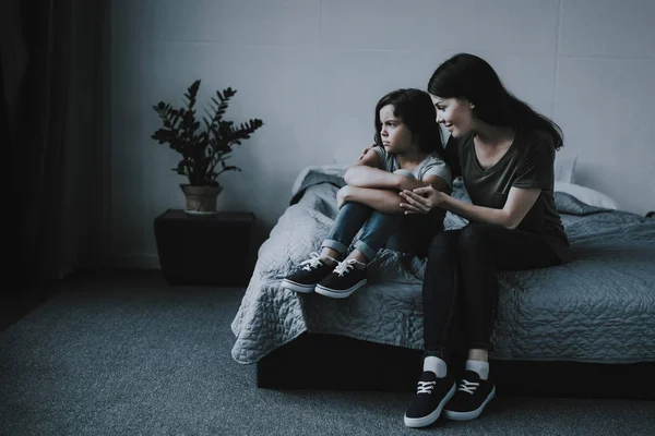 母亲拥抱安慰不安的女儿在卧室里 妇女纵向坐在灰色的床上拥抱黑发小女孩 T恤的孩子转身离开看侧裹腿 — 图库照片