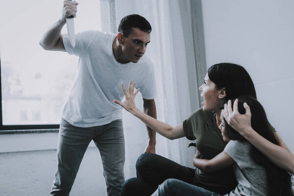 Mom Protects Girl From Threating Dad with Knife. Father Screams at Woman Who Hugs Scared Daughter Lying on Gray Bed Cries in Fear in Bright Bedroom. Quarrel and Family Violence Concept