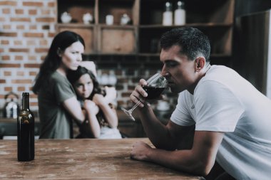 Anne ve çocuk, sarhoş Babam mutfakta bak. Adam ahşap tarzı tutun kadeh şarap elinde Modern odada sandalyede oturur. Karım çocuk ve bakışları kınayarak üzerinde koca sarılmak. Alkolizm kavramı