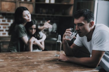 Karısı ve çocuğu evde sarhoş babasına bak. Adam Modern Mutfak tutun bardak alkol döner ve utanç ile uzak görünüyor sandalyeye oturur. Karısı Hugs kızı. Alkolizm kavramı