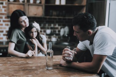 Karısı ve çocuğu evde sarhoş babasına bak. Adam Modern Mutfak tutun bardak alkol döner ve utanç ile uzak görünüyor sandalyeye oturur. Karısı Hugs kızı. Alkolizm kavramı