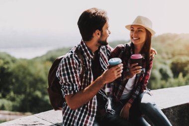 Çıkıntıya oturuyor ve kahve içme mutlu çift. Genç adam ve kadın ile birlikte Beton kenarında oturan sırt çantaları. Doğanın güzel manzarayı çift. Seyahat kavramı