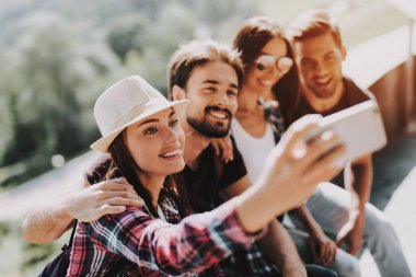 Genç gülümseyen insanlar oturmuş Selfie alarak Park. Sırt çantaları oturan Selfie yanında istimal Smartphone alarak birlikte genç arkadaşlarla grup. Seyahat etmek yaz zevk. İnsanlar ve dostluk kavramı