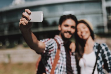 Selfie alarak sırt çantaları ile genç mutlu çift. Yakışıklı adam ve güzel kadın alarak Selfie yanında beyaz Smartphone kullanarak cam bina önünde. Yaz tatili zevk genç gezginler