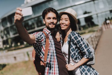 Selfie alarak sırt çantaları ile genç mutlu çift. Yakışıklı adam ve güzel kadın alarak Selfie yanında beyaz Smartphone kullanarak cam bina önünde. Yaz tatili zevk genç gezginler
