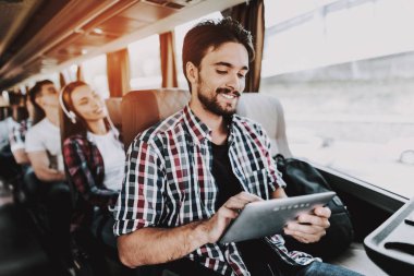 Dijital Tablet turist otobüsü kullanan gülümseyen adam. Genç yakışıklı tur otobüs yolcu koltuğunda oturan ve dokunmatik ekran cihaz tutan adam. Seyahat ve Turizm kavramı. Mutlu seyahat gezi