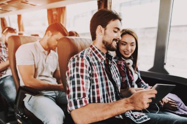 Gülümseyen iki tur otobüsü dijital Tablet kullanarak. Genç yakışıklı erkek ve tur otobüs yolcu koltuklarda oturan ve dokunmatik ekran cihaz kullanarak güzel kadın. Mutlu seyahat gezi