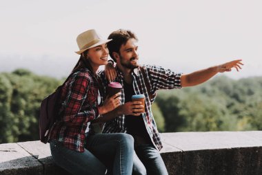 Çıkıntıya oturuyor ve kahve içme mutlu çift. Genç adam ve kadın ile birlikte Beton kenarında oturan sırt çantaları. Doğanın güzel manzarayı çift. Seyahat kavramı