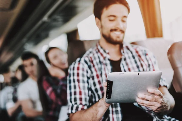 在旅游巴士中使用数字平板电脑的微笑者 年轻的帅哥坐在旅游巴士和持有触摸屏设备的乘客座位上 旅游和旅游概念 旅行中的愉快旅行者 — 图库照片