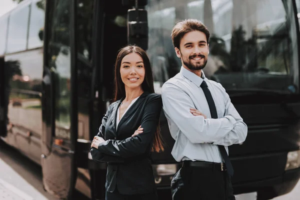 YYoung Smiling Business People Standing next to Bus. Confident Attractive Man and Beautiful Woman with Crossed Arms Standing in front of Tour Bus. Successful Professional Employees