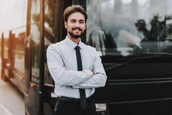 Young Smiling Businessman Standing in front of Bus. Confident Attractive Man wearing White Shirt and Black Tie with Crossed Arms Standing in front of Tour Bus. Successful Professional Employee