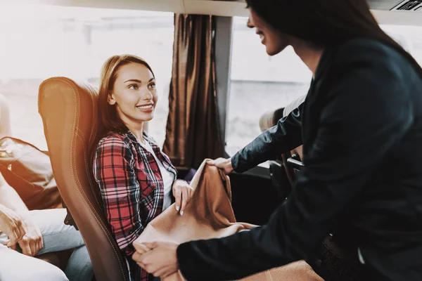 Female Tour Service Employee at Work on Tour Bus. Young Smiling Woman wearing Black Suit giving Blanket to Passenger. Traveling, Tourism and People Concept. People on Trip. Summer Vacation