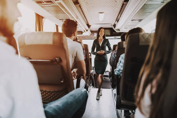 観光バスの仕事で女子ツアー サービス従業員 若い女性観光バスの乗客座席の間に立って笑っています の概念 旅行の人々 夏の休暇 — ストック写真