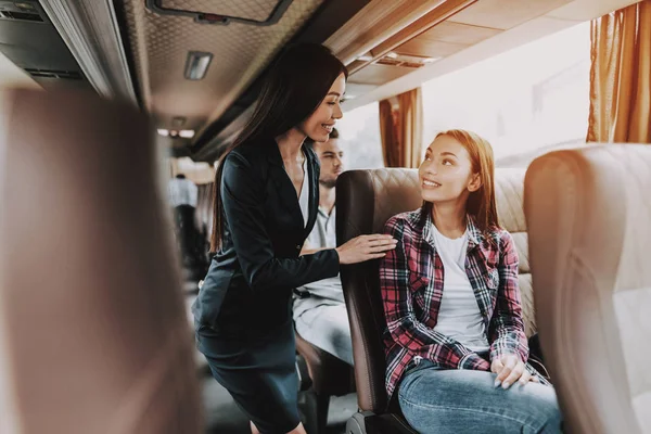 Female Tour Service Employee at Work on Tour Bus. Young Smiling Business Woman Standing between Passenger Seats and Talking to Woman. Traveling, Tourism and People Concept. People on Trip