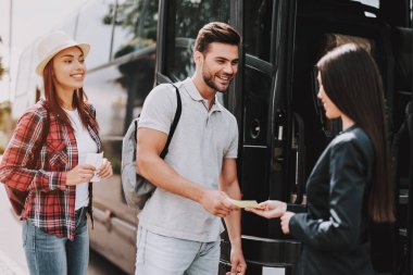 Tur hizmeti çalışan yolcu bilet alarak. Genç gülümseyen insanlarla sırt çantaları yatılı siyah Tur otobüste. Seyahat, turizm ve insanlar kavramı. Genç çift turist otobüsü girme