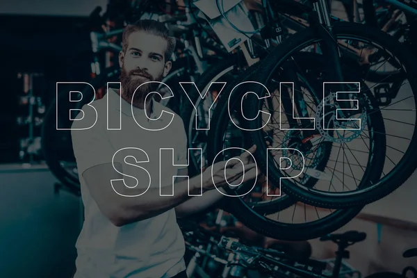 Bicycle Shop. Salesman Showing the Wheel of Bicycle. Young Beard Man. Hipster Man Looking in to Camera. Different Bicycles on Background of Man. Man Sales the Bicycles.