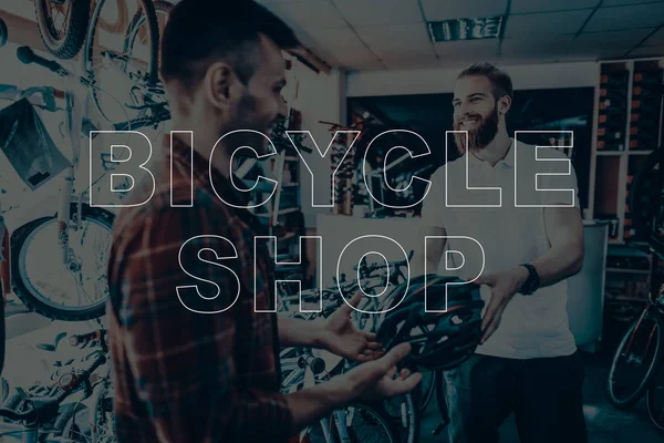 Bicycle Shop. Salesman Showing Bicycle Helmet to Customer. Customer Choosing the Helmet on His Bike. Hipster Male Salesman. People Happy and Smiling. Man Sales the Bicycles Equipment.