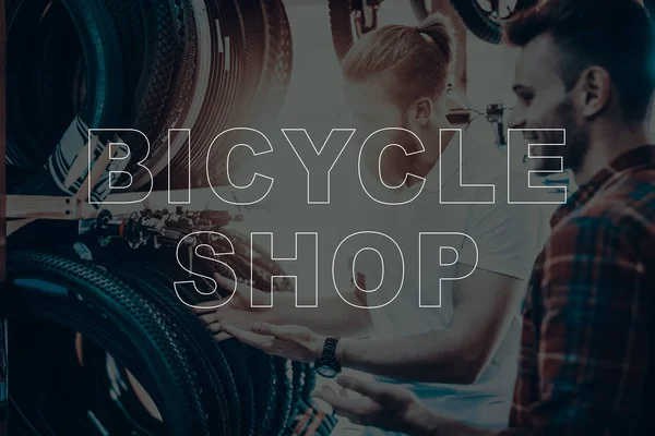 Bicycle Shop. Salesman Showing Bicycle Tyres to Customer. Customer Choosing the Tyre on His Bike. Hipster Male Salesman. Customer Happy and Smiling. Man Sales the Bicycles Equipment.