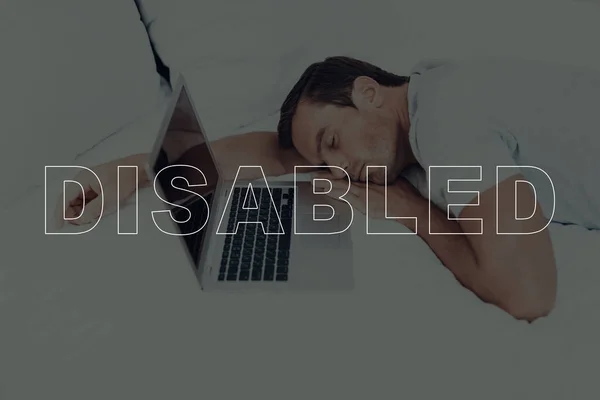 Disabled Man. Man is Lying on Bed. Man with Closed Eyes. Man is Sleeping. Laptop Computer Lying on Bed. Tired Man. Adult Caucasian Brunette Man. Bed with Pillows. Man Located in Bedroom.